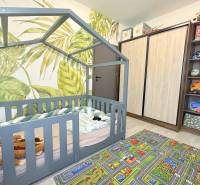 Children's room with a house-shaped bed, leaf wallpaper, and a play carpet.