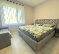 A bedroom in a family house with a bed, sofa, television, and curtains on the window.