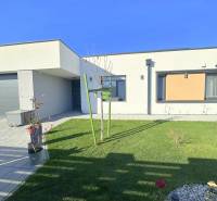 A family house in Mosonmagyaróvár with a green lawn, stone decor, and elegant flowers in pots.