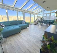 Family house with a glass veranda, sofas, plants, and a wooden decor floor.