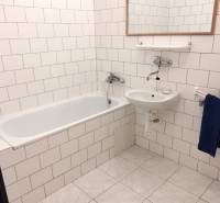 A bathroom in a studio apartment with a bathtub, sink, and white tile cladding.