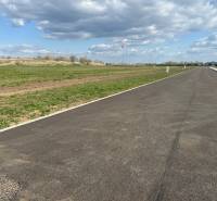 An asphalt road leading between green commercial properties in Trnava under a cloudy sky.