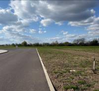 Flat commercial plots in Trnava with an asphalt road and clear skies.