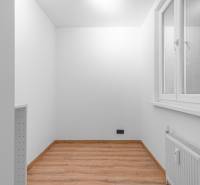 A white room with a window, a wooden decor floor, and a radiator in a studio apartment.
