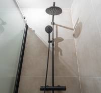 Shower head and square bathtub in the bathroom of a studio apartment.