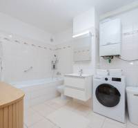 Bathroom in a 2-room apartment with a bathtub, washing machine, and light tiles.