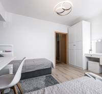 A bedroom in a two-room apartment with white furniture, wooden decor flooring.