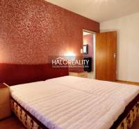 A room in a 2-room apartment with a bed, nightstands, and decorative red wallpaper.