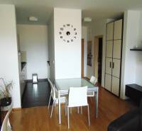 Interior of a 1-bedroom apartment with a dining table, wood-patterned flooring, and a clock on the wall.