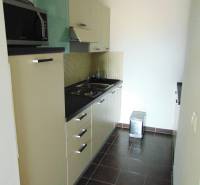 A kitchen in a studio apartment with dark tiles, cabinets, and a microwave.