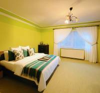 A bedroom in a family house with a bed, green walls, and white curtains.