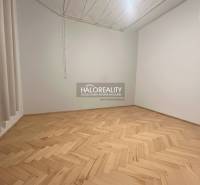 An empty room of a three-room apartment with a wood-patterned floor and pendant lights.