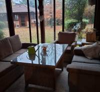 A glazed terrace of a family house with comfortable seating and a view of the garden.