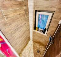 A shower corner with wood decor in a cottage interior, complemented by mosaic tiles and a window.