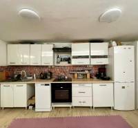 A kitchen in a cottage with white cabinets, brick cladding, and wood-patterned flooring.