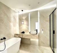 A bathroom with a freestanding bathtub in a 4-room apartment, with light tiles and a mirror.