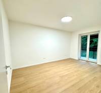 A room in a 4-room apartment with a wood-patterned floor and a large window.