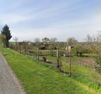 Recreational plots in Drahovece with a road, fence, trees, and maintained lawn along the access road.