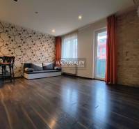 Living room in a two-room apartment with patterned wallpaper and wood-decor flooring.