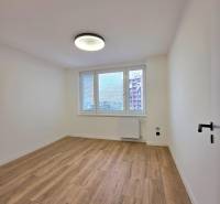 A room in a 3-room apartment with a wood-patterned floor and a window with a radiator.