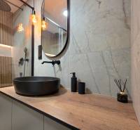 A bathroom in a 3-room apartment with a dark wash basin and a floor with a wood decor.