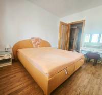 A bedroom with an orange bed, a nightstand, and a wooden decor floor in a three-room apartment.