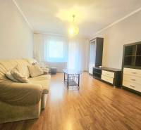 Living room of a three-room apartment with a wooden decor floor, a sofa, and a glass table.