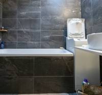 A bathroom with a bathtub and dark tiles in a 2-room apartment, equipped with a washing machine.