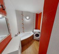 A bathroom in a 3-room apartment with orange and white tiles, a bathtub, and a washing machine.
