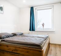 Bedroom with wood-patterned flooring and a bed in a two-room apartment, blue curtain on the window.