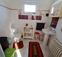 A bathroom with a window in a family house, white sanitary ware, patterned tiles, red rugs.
