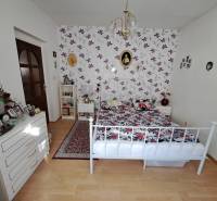A bedroom in a family house with floral wallpaper, a metal bed, and a wooden decor floor.