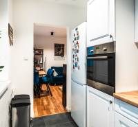 The kitchen of a two-room apartment with white cabinets, appliances, and a view into the dining room.