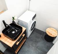 A bathroom in a 2-room apartment with a black sink, a washing machine, and wooden decor.
