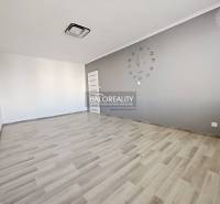 A room with a clock and a wooden decor floor in a two-room apartment.