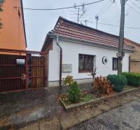 A family house in Komárno with a gable roof and an entrance gate, a front garden with shrubs.