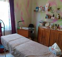 A room in a family house with a massage table, a writing desk, and shelves with books.