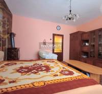 Interior of a family house with wooden furniture, a carpet, and a bed with a colorful throw.
