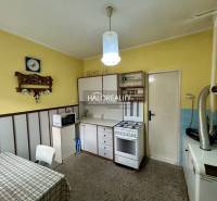 A kitchen in a family house with yellow walls, white furniture, and a carpeted surface.