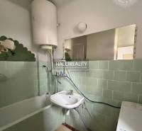 A bathroom in a 3-room apartment with a bathtub, sink, washing machine, and green wall tiles.