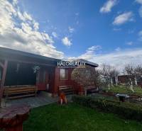 A wooden cottage in the gardens of Spišská Nová Ves with benches and a flower bed.