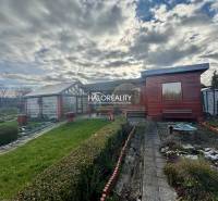 A wooden cottage in the gardens in Spišská Nová Ves, surrounded by a manicured lawn and shrubs.