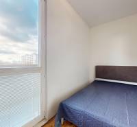 A room in a 3-room apartment with a bed, a wooden decor floor, and a large window.