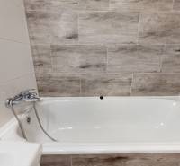 A bathtub in the bathroom of a 3-room apartment with tiles featuring a wood decor.