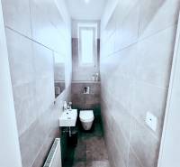 Narrow toilet with a window, sink, and ceramic tiles. Offices Reality Kováčová.