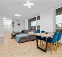 Living room in a three-room apartment with a wooden decor floor, a large sofa, and a dining table.