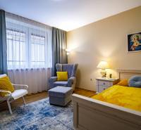 A room in a family house with a bed, a chair, a table, and a floor with a wooden decor.