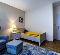 A room in a family house with an armchair, a bed, a nightstand, and a floor with a wooden decor.