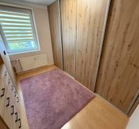 A wardrobe with wooden decor cabinets, a pink carpet, a window with blinds in a 4-room apartment.