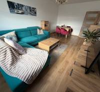Living room of a 4-room apartment with a turquoise sofa, wooden decor flooring, and a dining table.